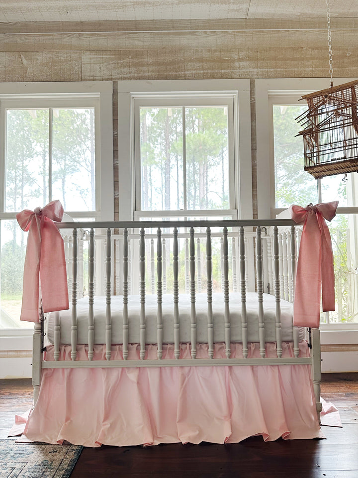 Sisters Pink farmhouse crib bedding set with a gathered crib skirt and two large pink crib bows on a white spindle crib