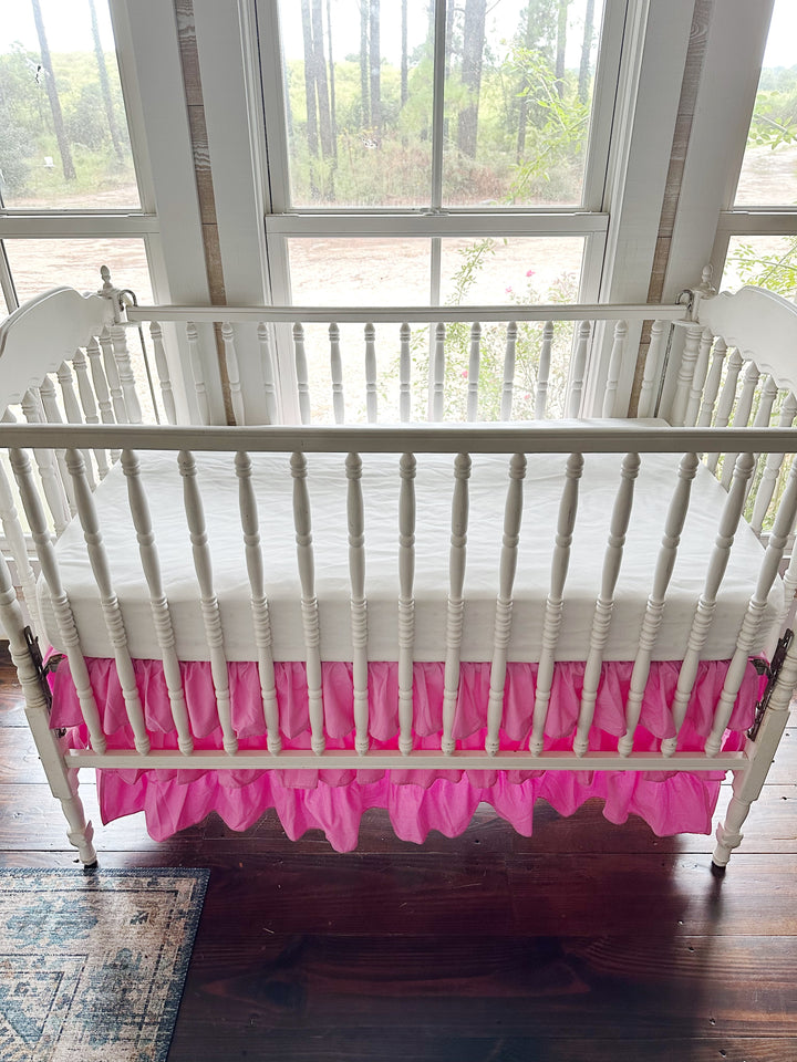 View over the crib rail of the parfait pink ruffle tiers stacked beneath a white crib mattress