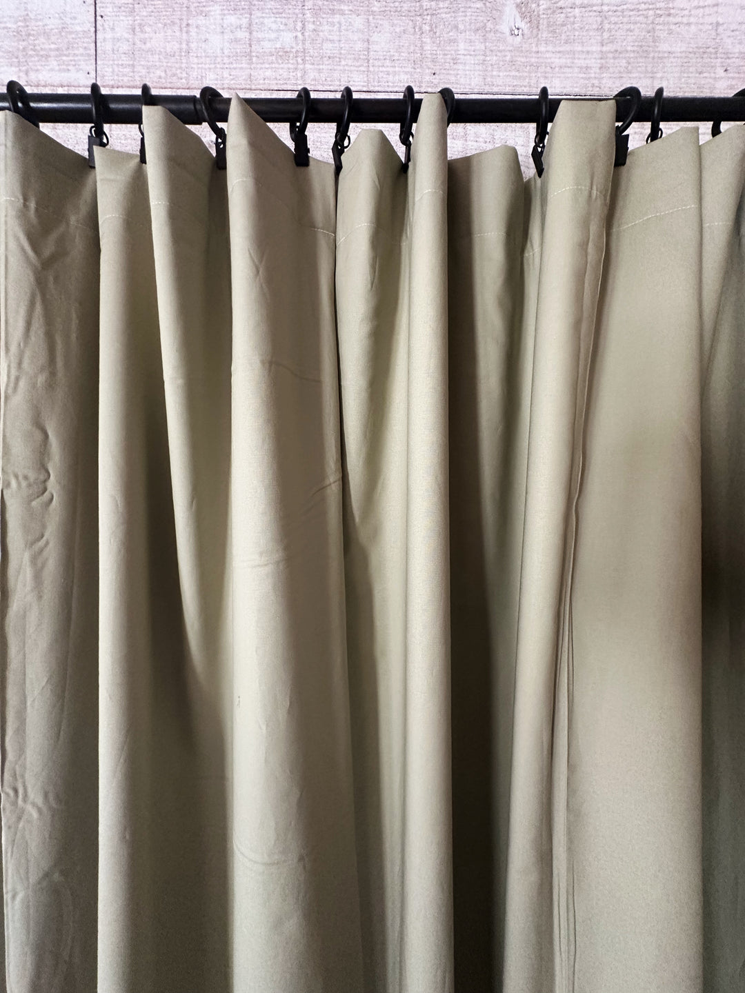 Close view of the sage curtain tops gathered into folds beneath a row of black curtain rings