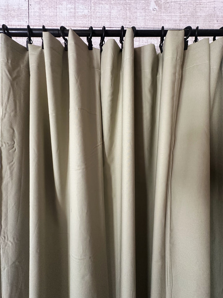 Close view of the sage curtain tops gathered into folds beneath a row of black curtain rings