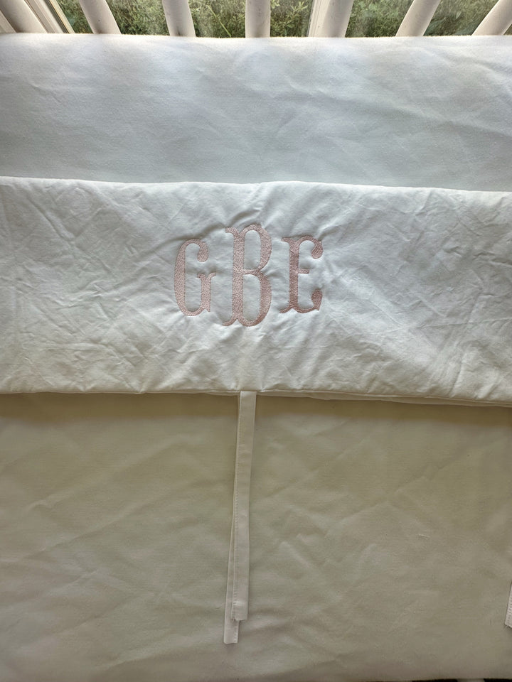 Plain white rail cover on the crib rail in a pine-panelled nursery with a hanging birdcage