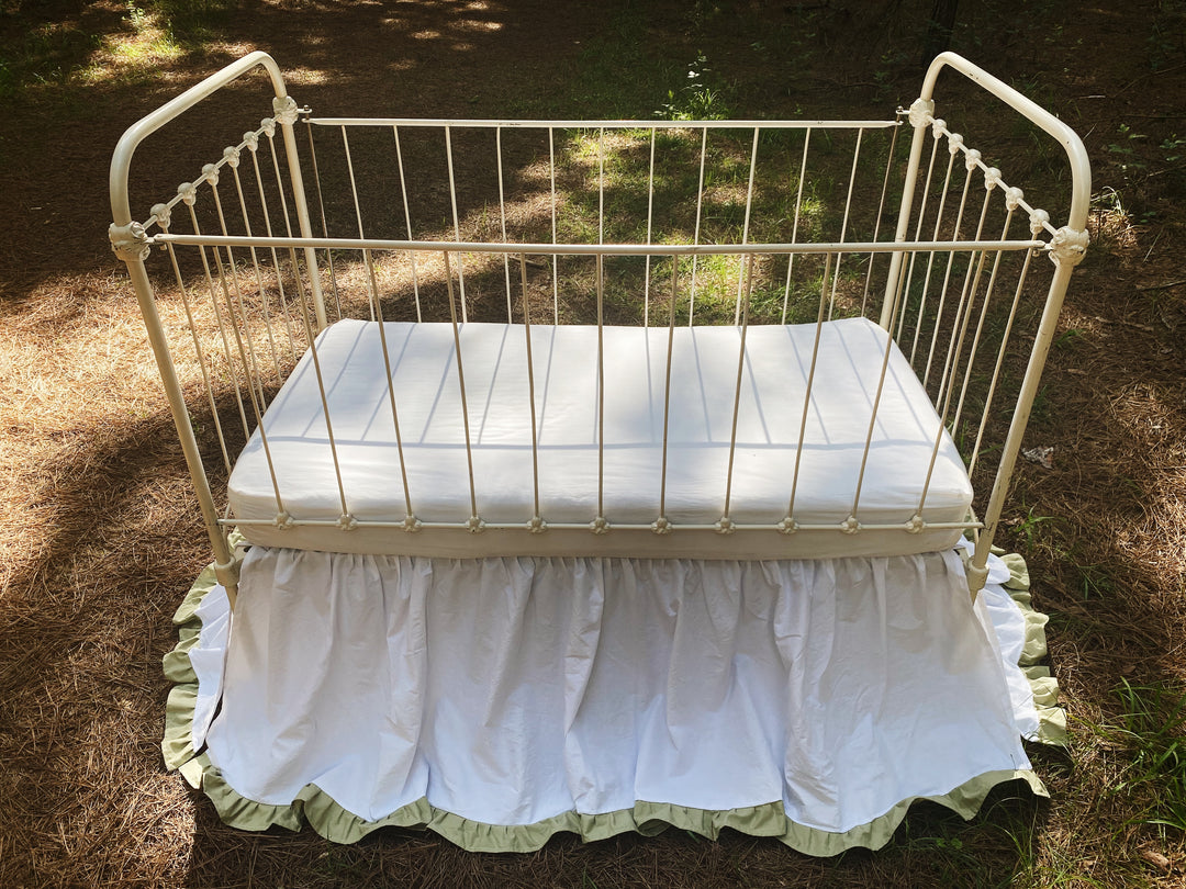 White and sage two-tone ruffled crib skirt on vintage iron crib, overhead view showing full gathered coverage