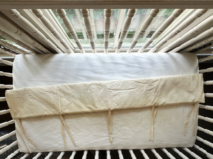 Overhead view of a Natural short rail cover folded over the end top rail of a spindle crib