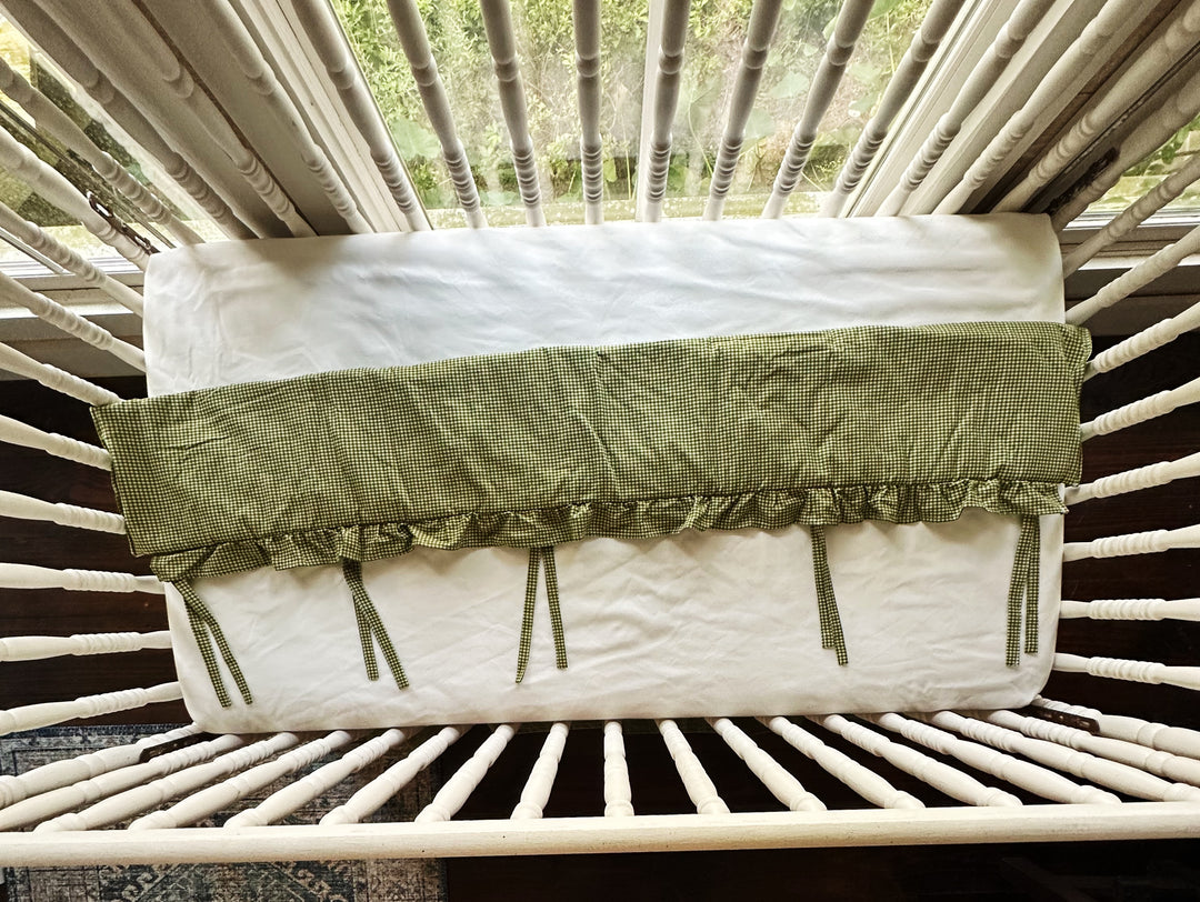 Overhead view of the green gingham crib rail cover showing its full length and tie placement
