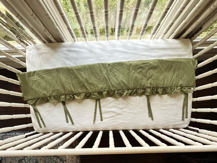Overhead view of the green gingham crib rail cover showing its full length and tie placement
