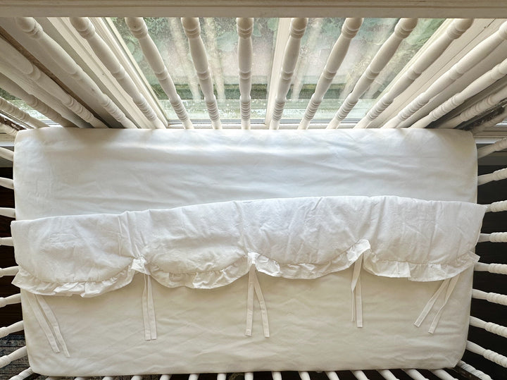 Overhead view of the white scalloped crib rail cover showing the scalloped hem and evenly spaced ties