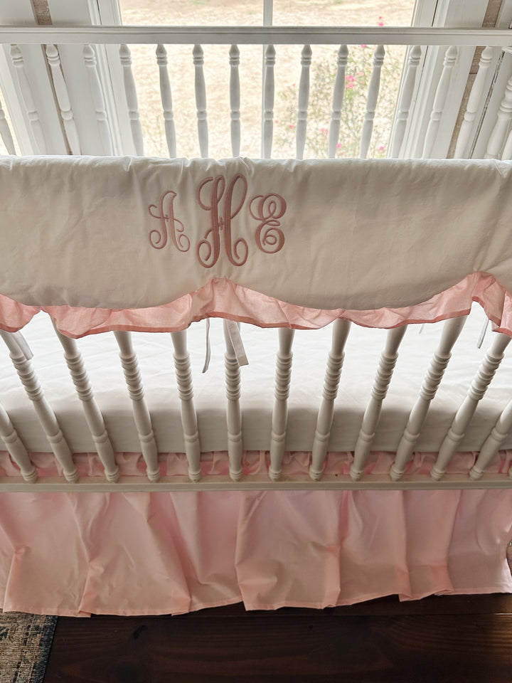Scalloped crib rail cover with a pink script monogram and Sisters Pink ruffle above a gathered pink crib skirt