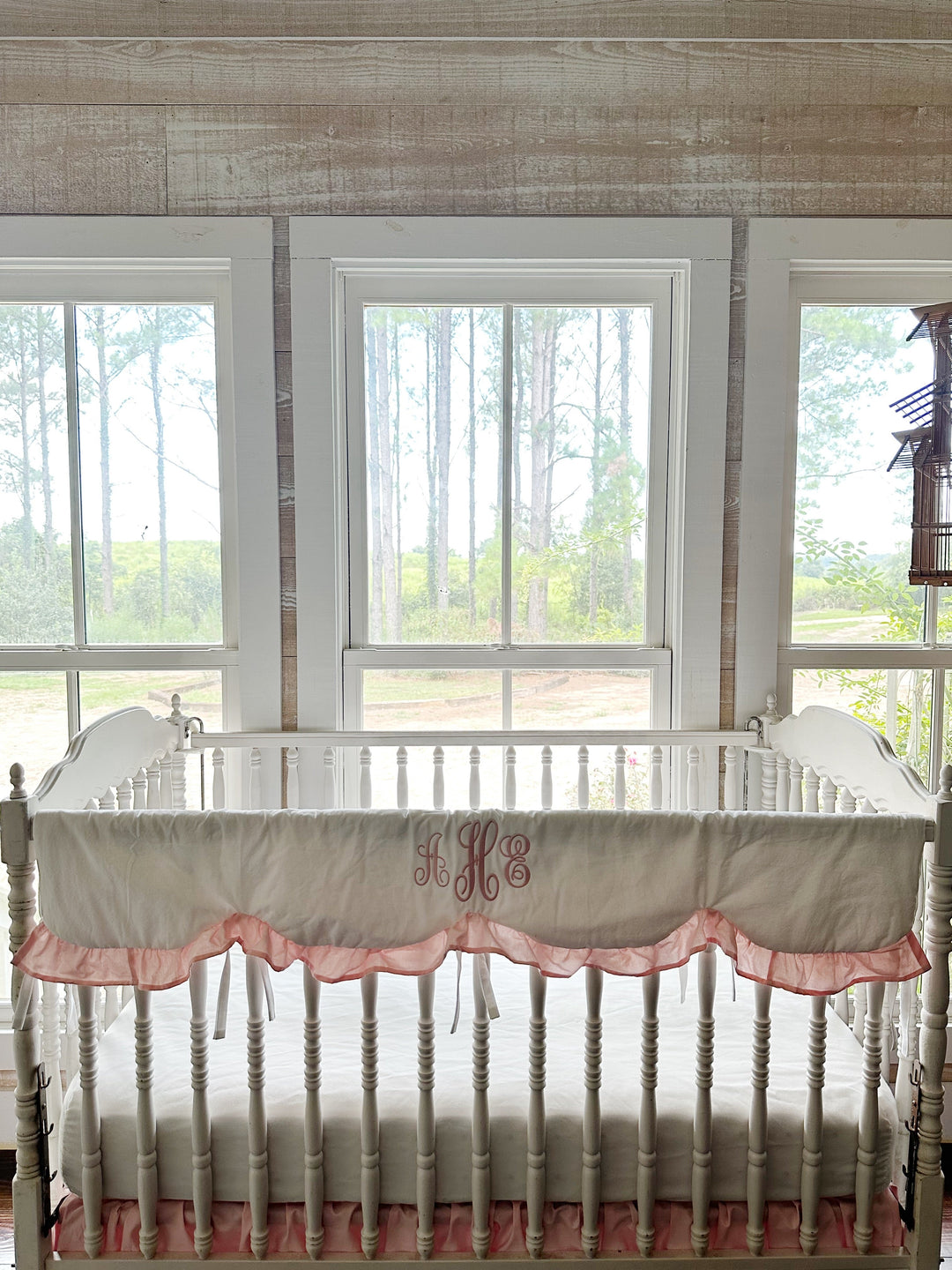 White scalloped crib rail cover with a Sisters Pink ruffle and pink monogram on a white spindle crib