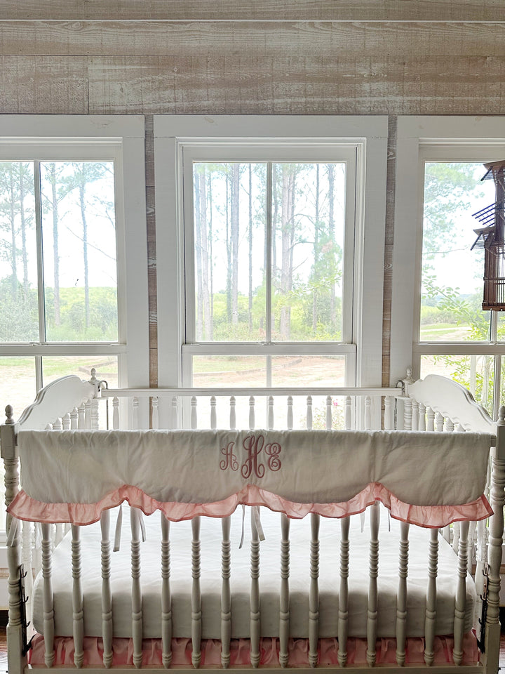 White scalloped crib rail cover with a Sisters Pink ruffle and pink monogram on a white spindle crib