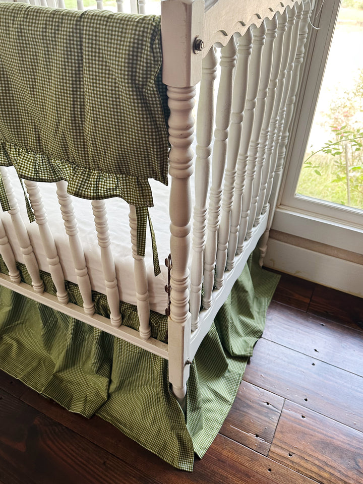 Corner detail of green gingham crib rail cover tied to a white crib rail above the crib skirt