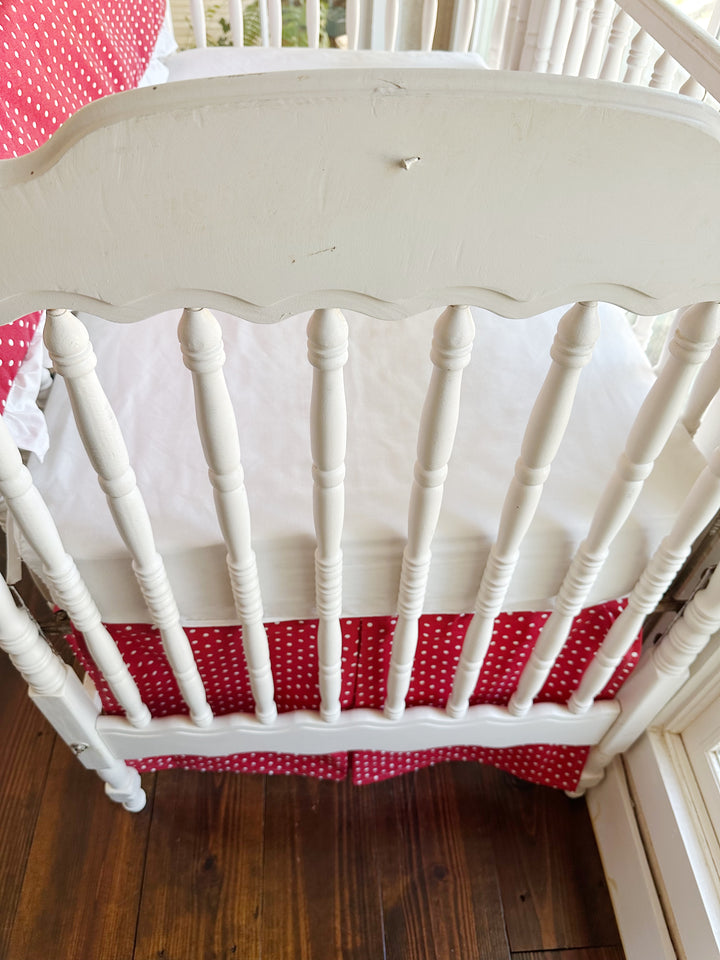 The scalloped headboard and turned spindles above the pleated red polka dot skirt