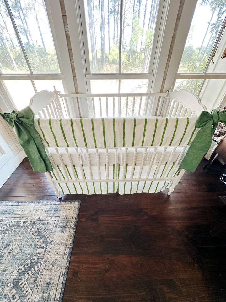 Looking down into the crib at the striped rail cover, white sheet and striped tailored skirt