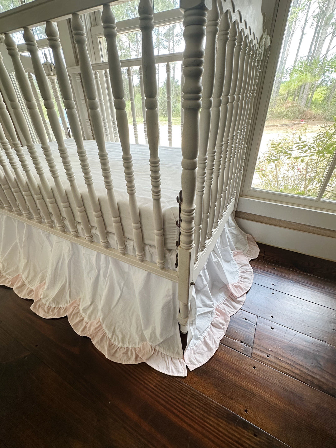 Corner of the crib where two scalloped skirt panels meet above a dark wood floor