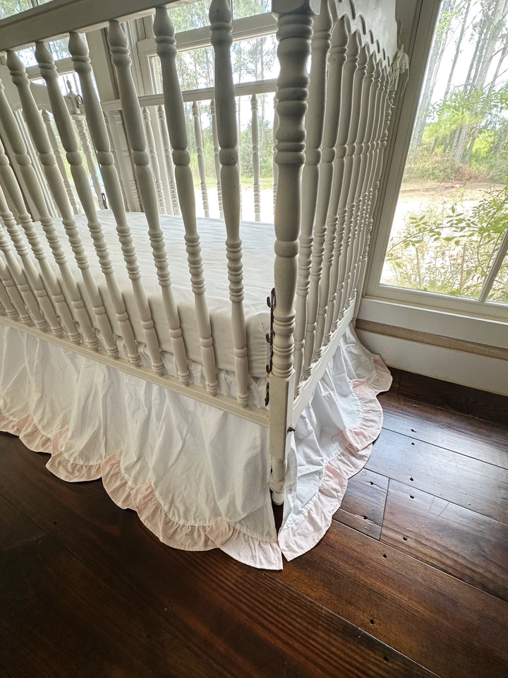 Corner of the crib where two scalloped skirt panels meet above a dark wood floor