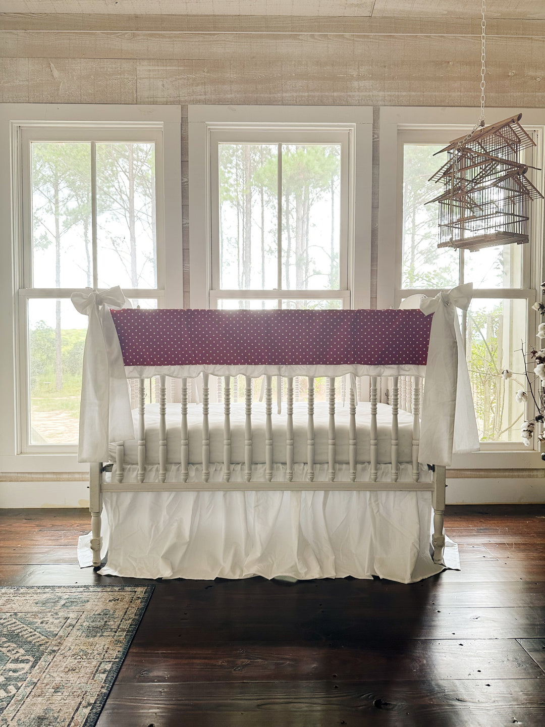The red polka dot crib set in a pine-paneled nursery with three windows and a hanging birdcage