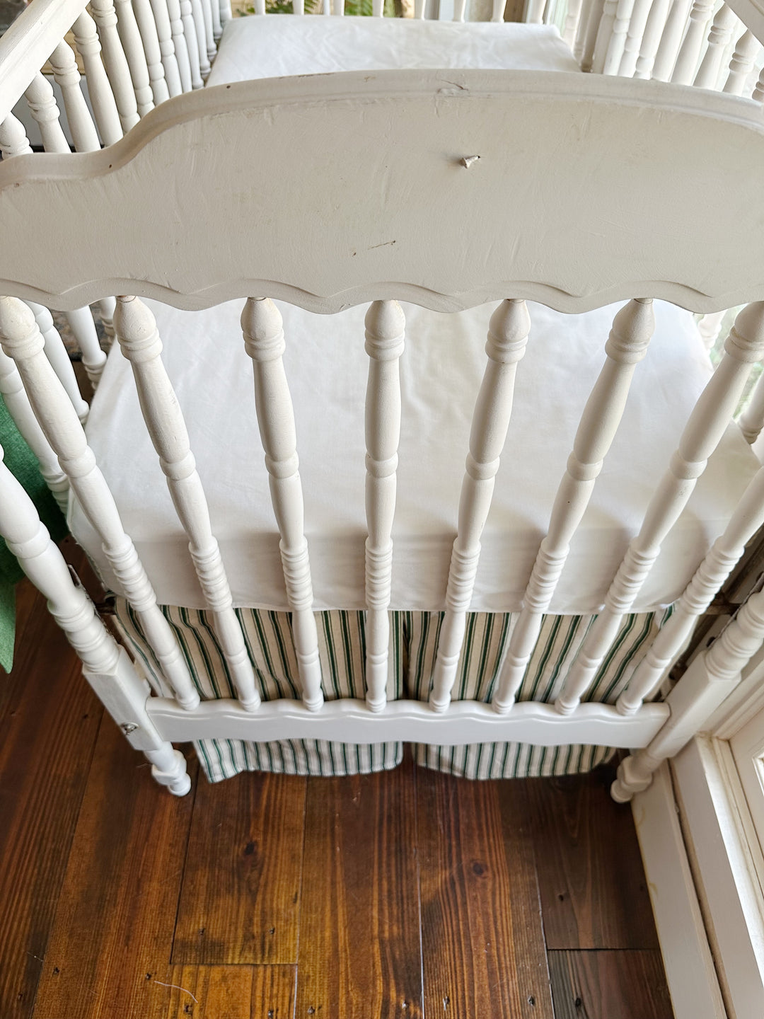 The scalloped end panel and turned spindles above the ticking skirt's center pleat