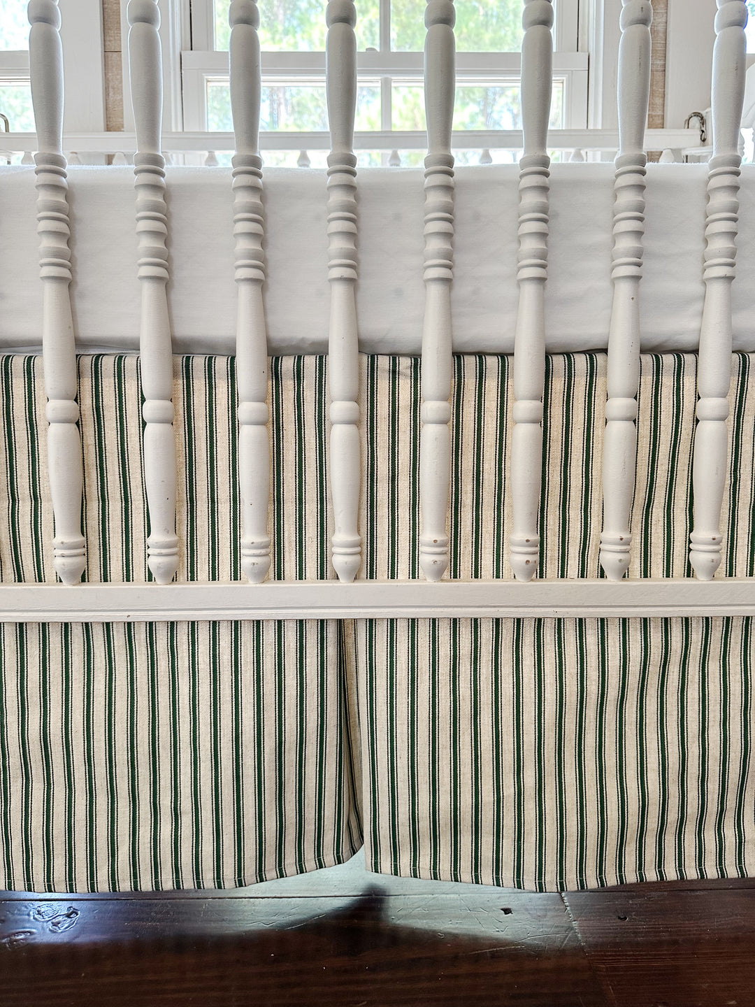 The ticking skirt filling the frame through the crib spindles — green stripes on natural and the inverted center pleat