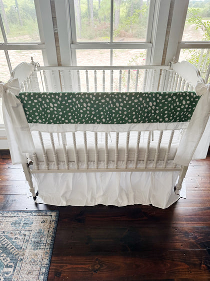 Green and white dot ruffled crib rail cover with a white farmhouse skirt and two white bows on a spindle crib