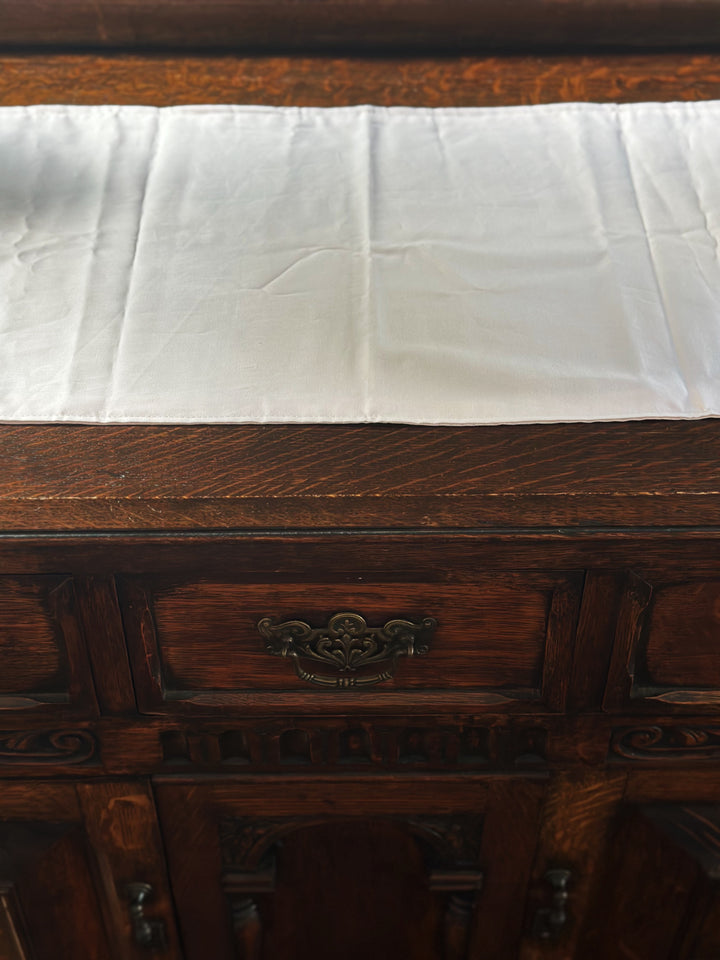 Baby pink runner across the top of a quarter-sawn oak dresser, above a drawer with an ornate brass pull