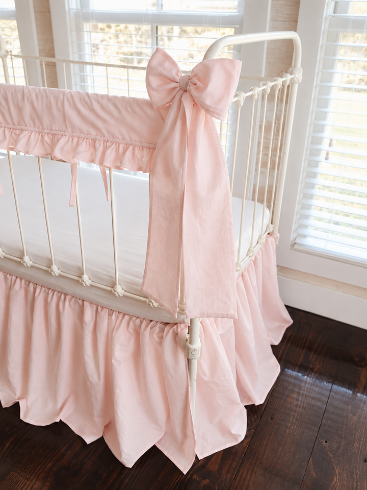 Close view of a Ballet Slipper Pink bow knotted at the crib post above the ruffled rail cover and farmhouse skirt