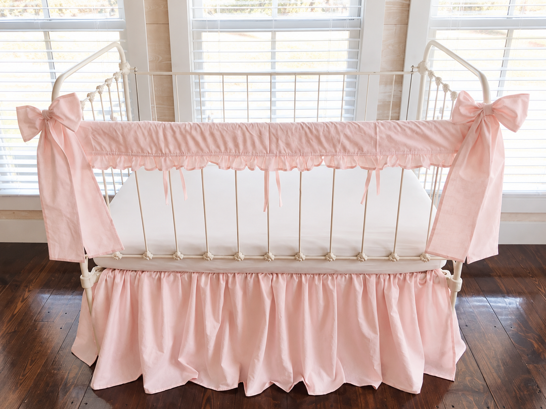 Straight-on view of the pink ruffled rail cover with slim ties between the spindles and a bow at each post