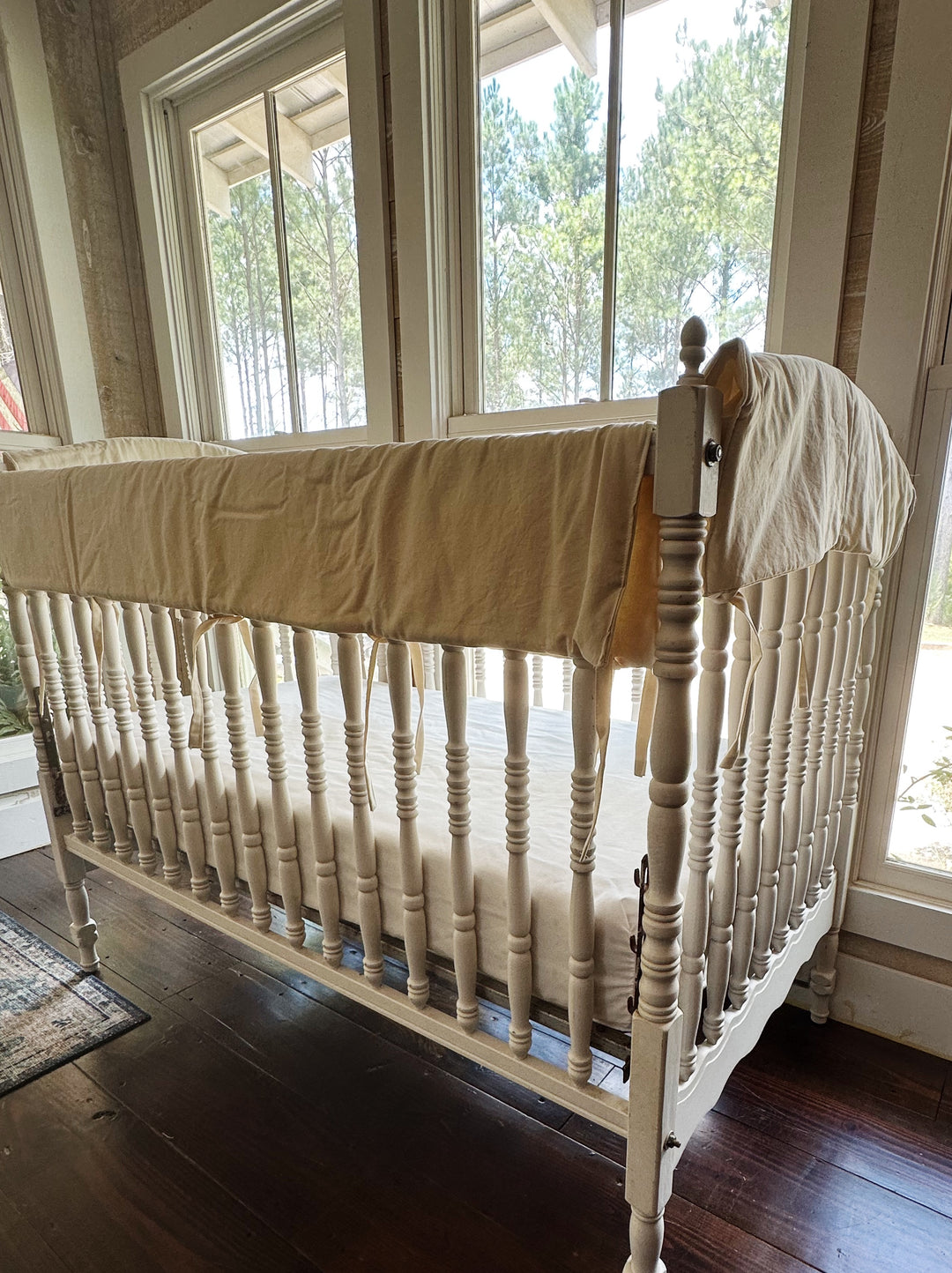 Neutral beige crib rail cover on the long top rail of a Jenny Lind style crib in a sunlit nursery