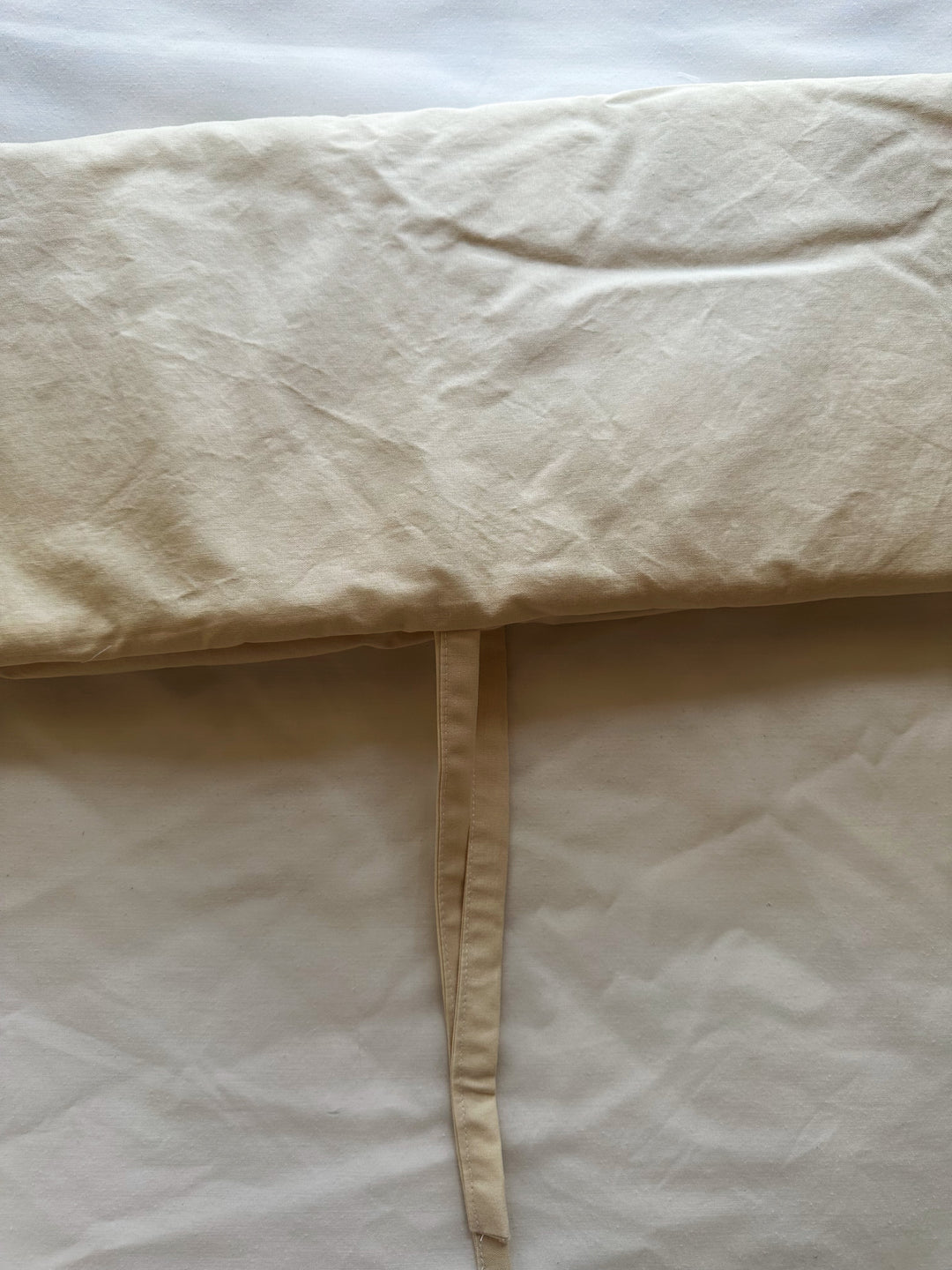 Close-up of the sewn edge and cotton tie on a Natural crib rail cover in warm beige