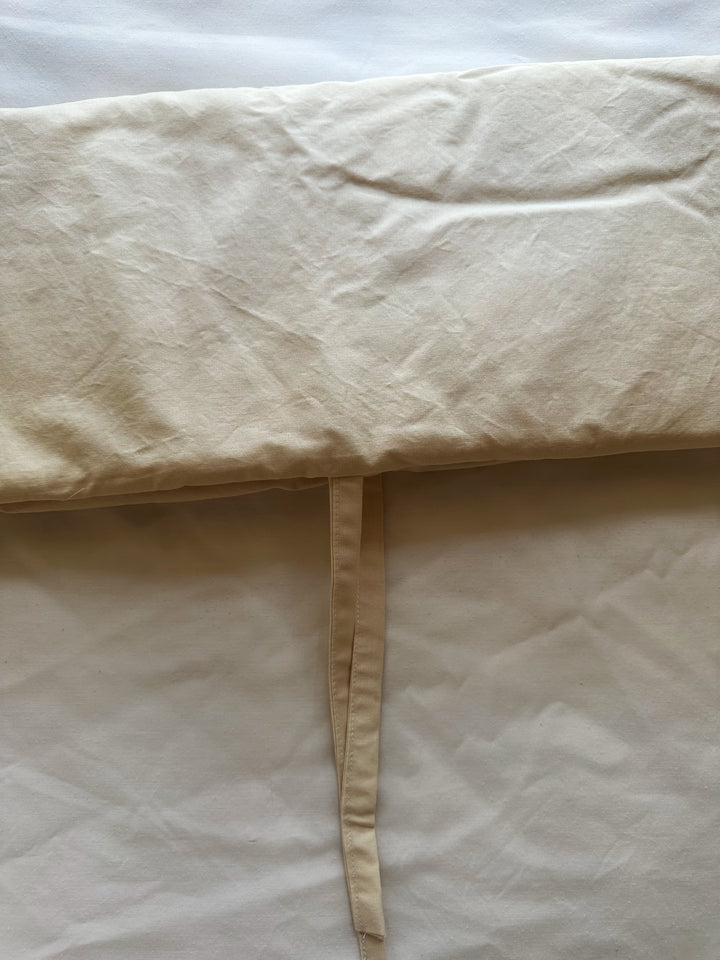 Close-up of the sewn edge and cotton tie on a Natural crib rail cover in warm beige