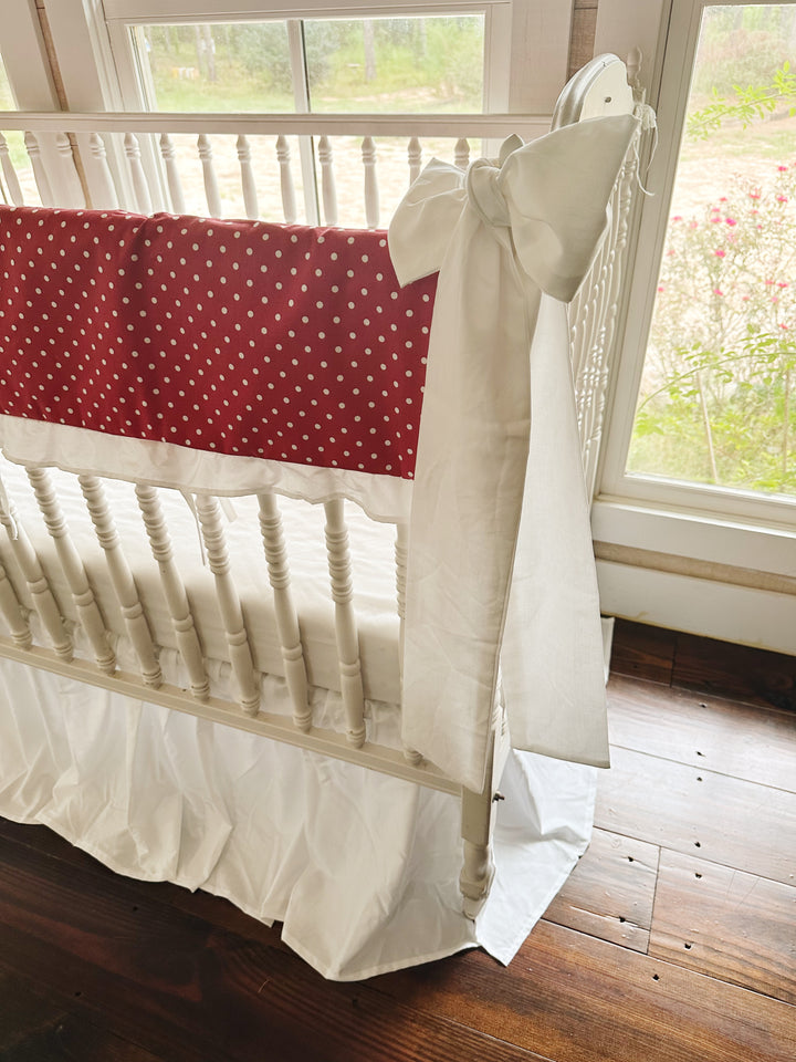 Side view of the polka dot print running the length of the long crib rail above the white skirt