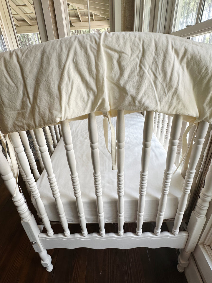 Short end rail of the crib wrapped in the ivory cover above a white fitted crib sheet