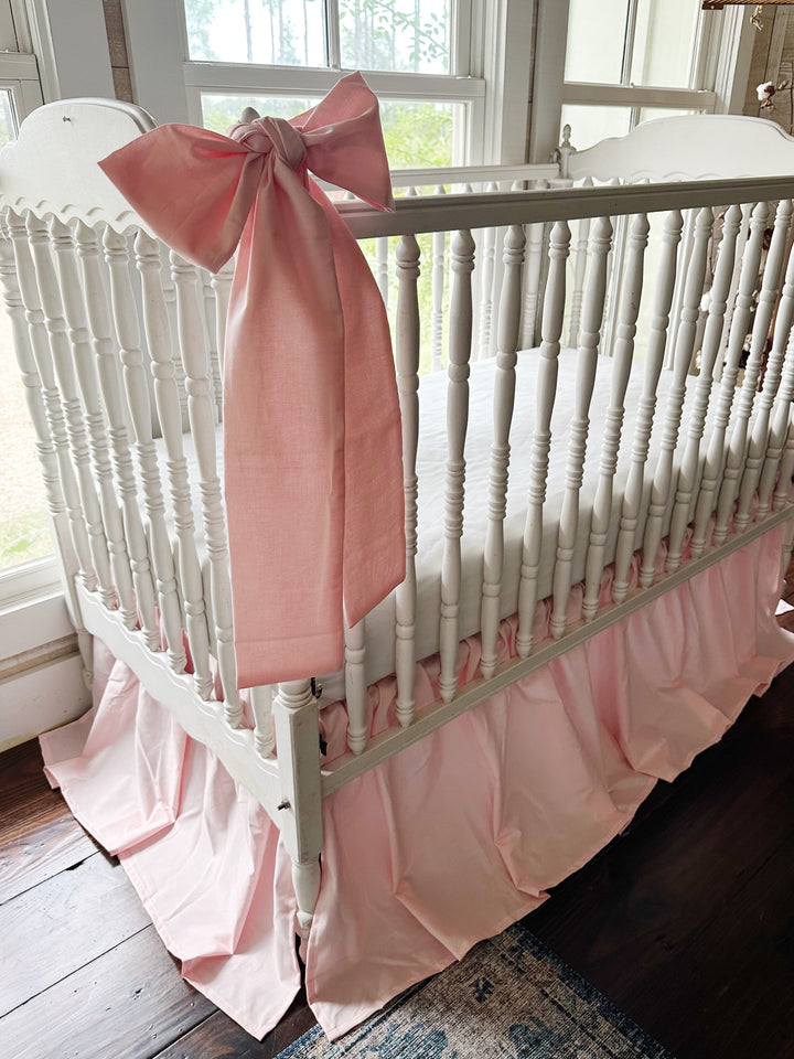 Large Sisters Pink crib bow tied at a crib corner post above the pleated farmhouse crib skirt