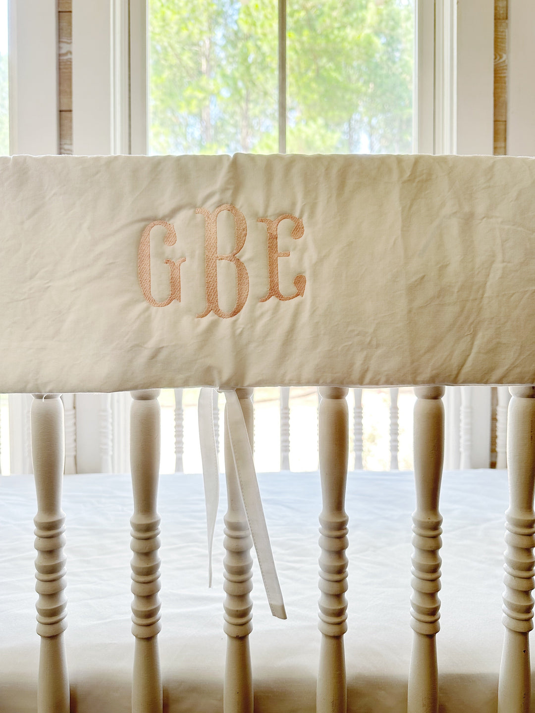 Close view of the pink three-letter monogram stitched on the white cotton rail cover