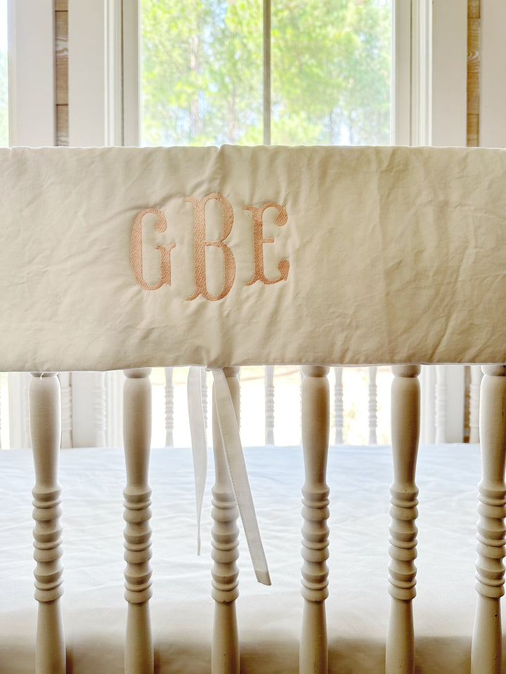 Close view of the pink three-letter monogram stitched on the white cotton rail cover