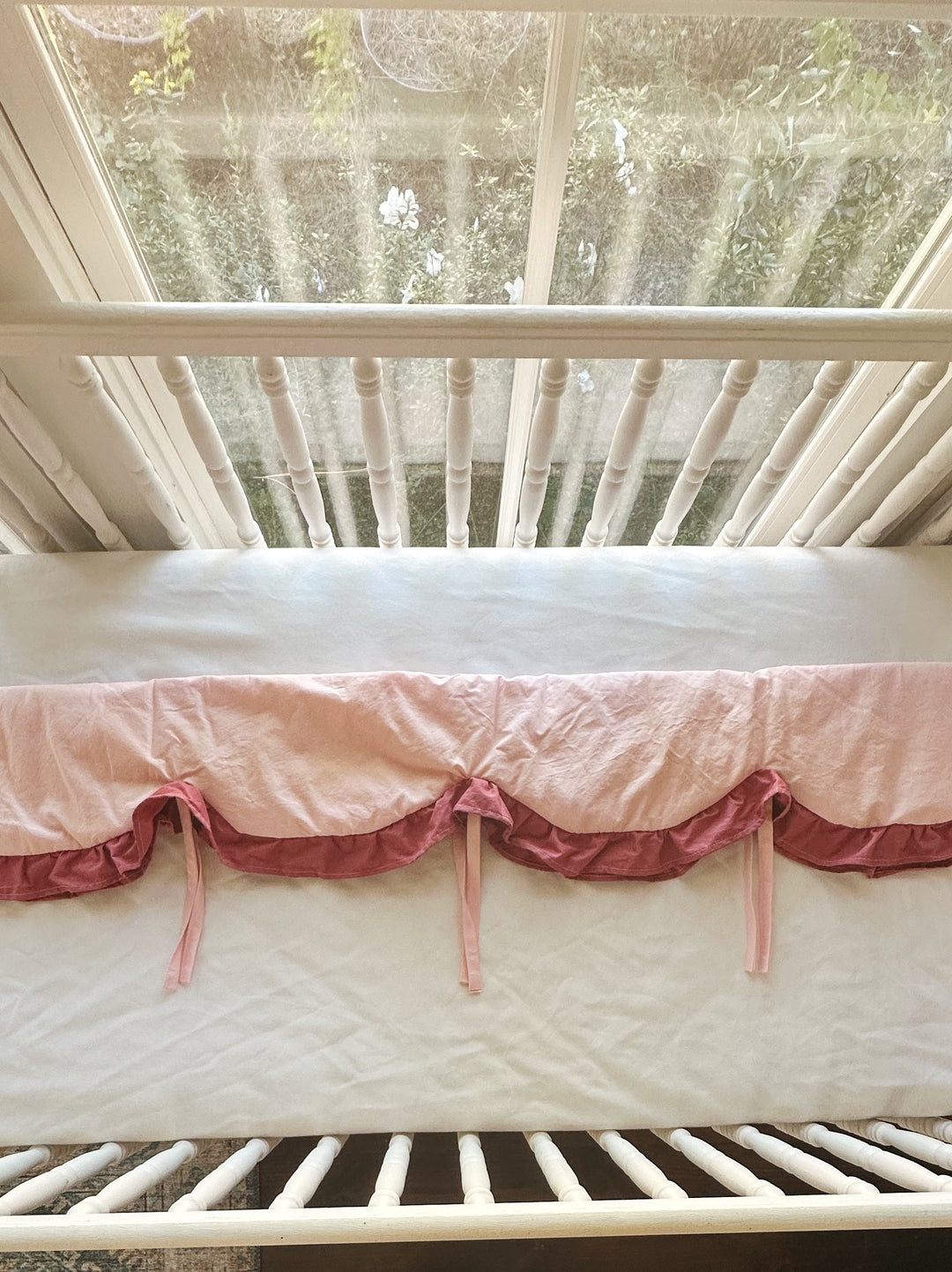 Looking down on the rail cover over the crib rail, pink ties hanging between the scallops