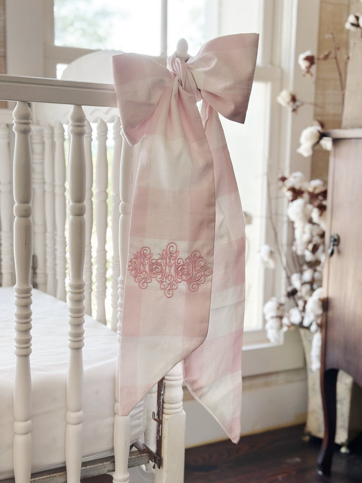 Pink buffalo check bow on the crib post with cotton stems and an antique cabinet behind