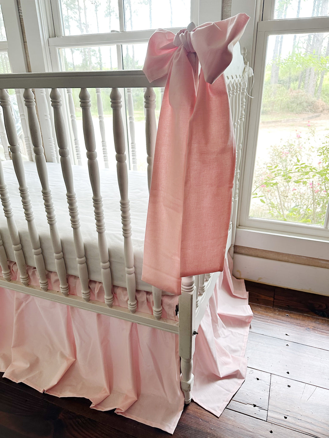Close view of a Sisters Pink crib bow sash draping over the crib rail beside the gathered crib skirt