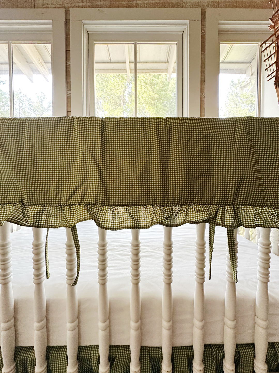 Close-up of ruffled green gingham crib rail cover with tiny ties along the crib railing
