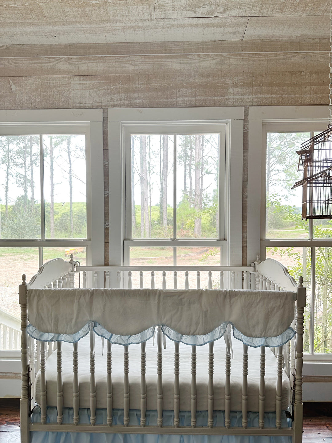 Wide nursery view with the scalloped rail cover on the crib beneath three bright windows