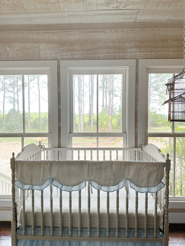 Wide nursery view with the scalloped rail cover on the crib beneath three bright windows