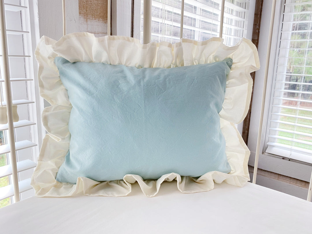 Mist and ivory ruffled crib pillow propped against the rail of an antique iron crib