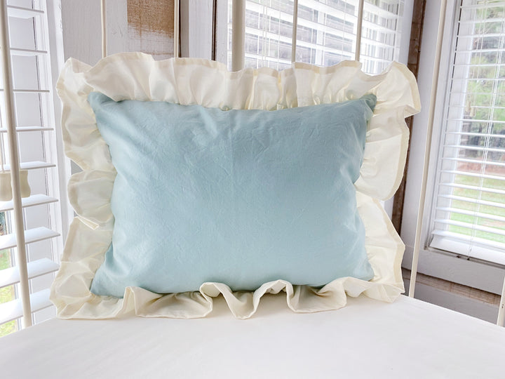 Mist and ivory ruffled crib pillow propped against the rail of an antique iron crib