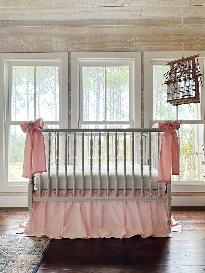 Sisters Pink crib skirt and bow set styled in a farmhouse nursery with pine views and a hanging birdcage