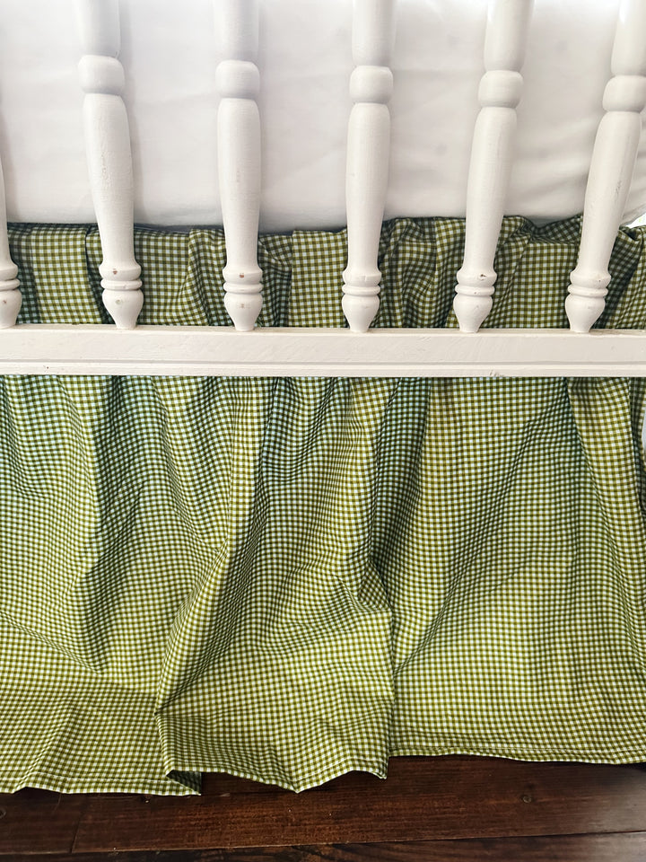Gathered pleats of the pine green gingham farmhouse crib skirt behind white crib spindles