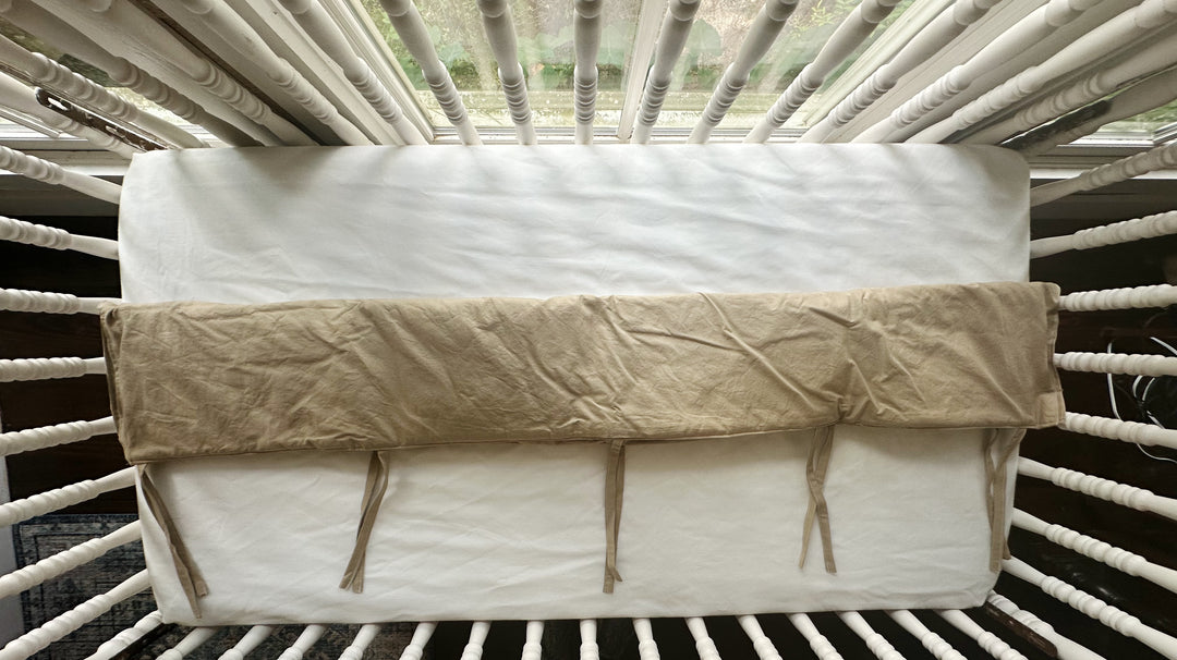 Top view of oatmeal crib rail cover tied over the crib top rail - High Cotton Textile