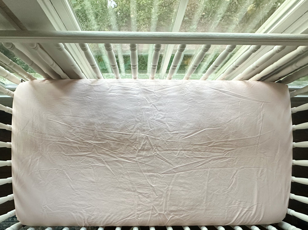 Sisters Pink fitted crib sheet seen from above, fitted snugly over the mattress in a white spindle crib - High Cotton Textile