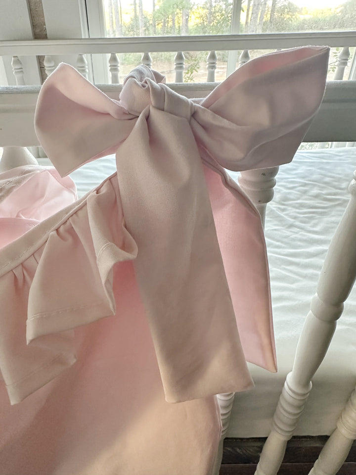 Close-up of a long pink sash bow tied around the crib rail beside the ruffle
