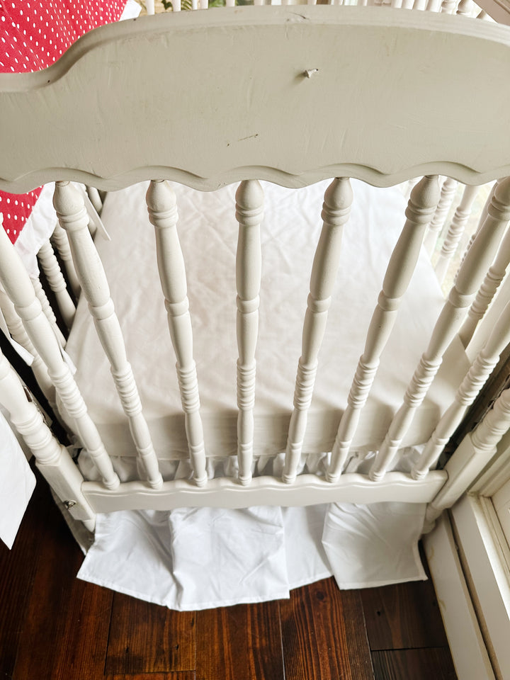 Looking down past the scalloped headboard at the white sheet and gathered white skirt