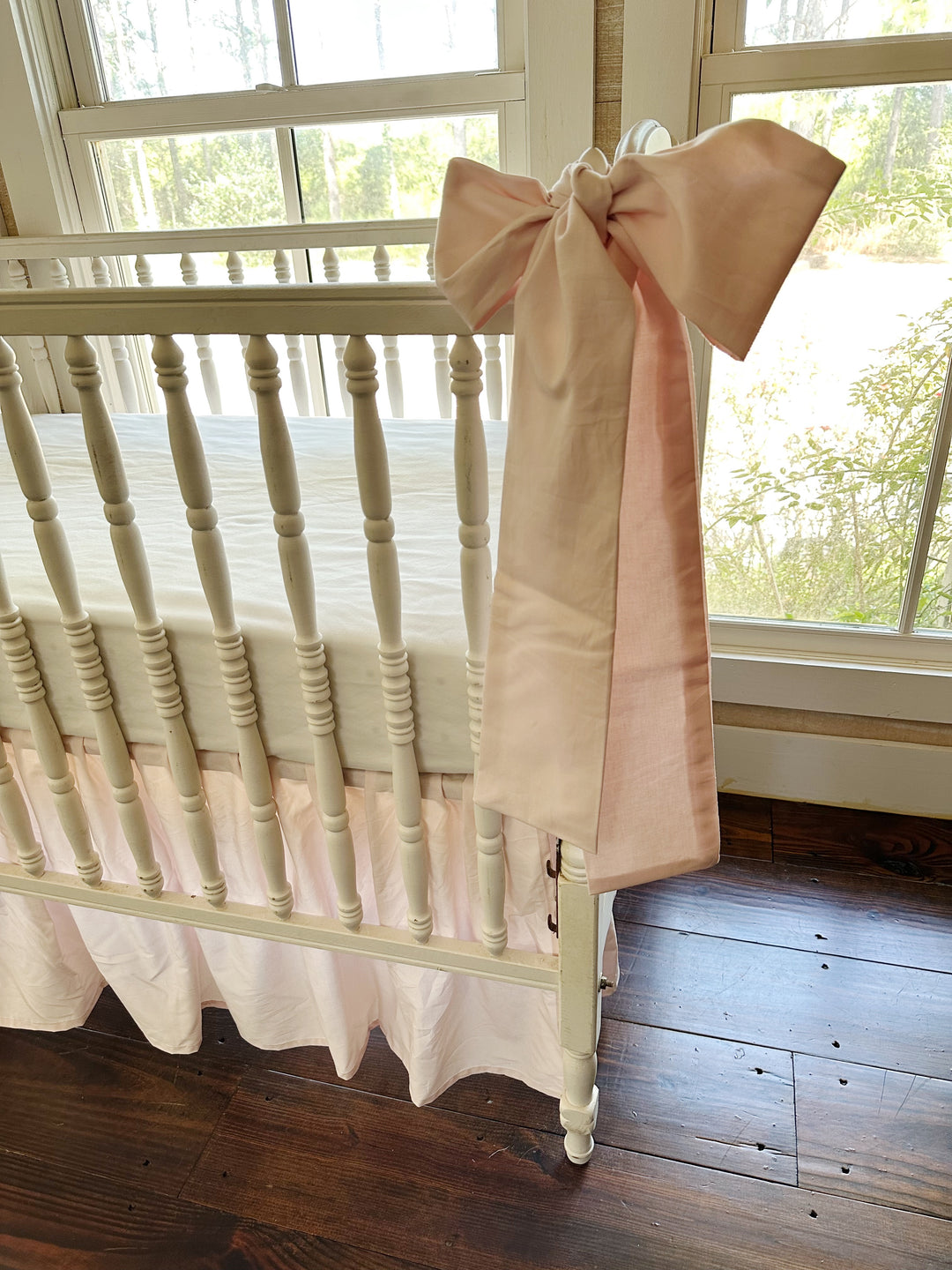 Side view of a pink bow at the rail with the soft pink skirt gathering beneath the mattress