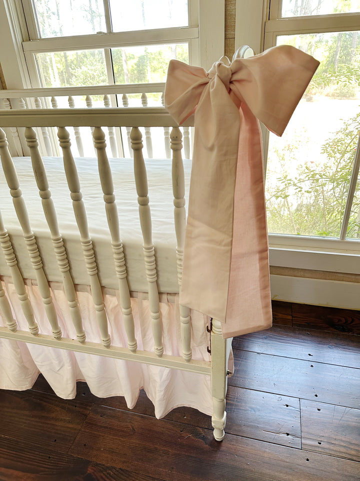 Side view of a pink bow at the rail with the soft pink skirt gathering beneath the mattress