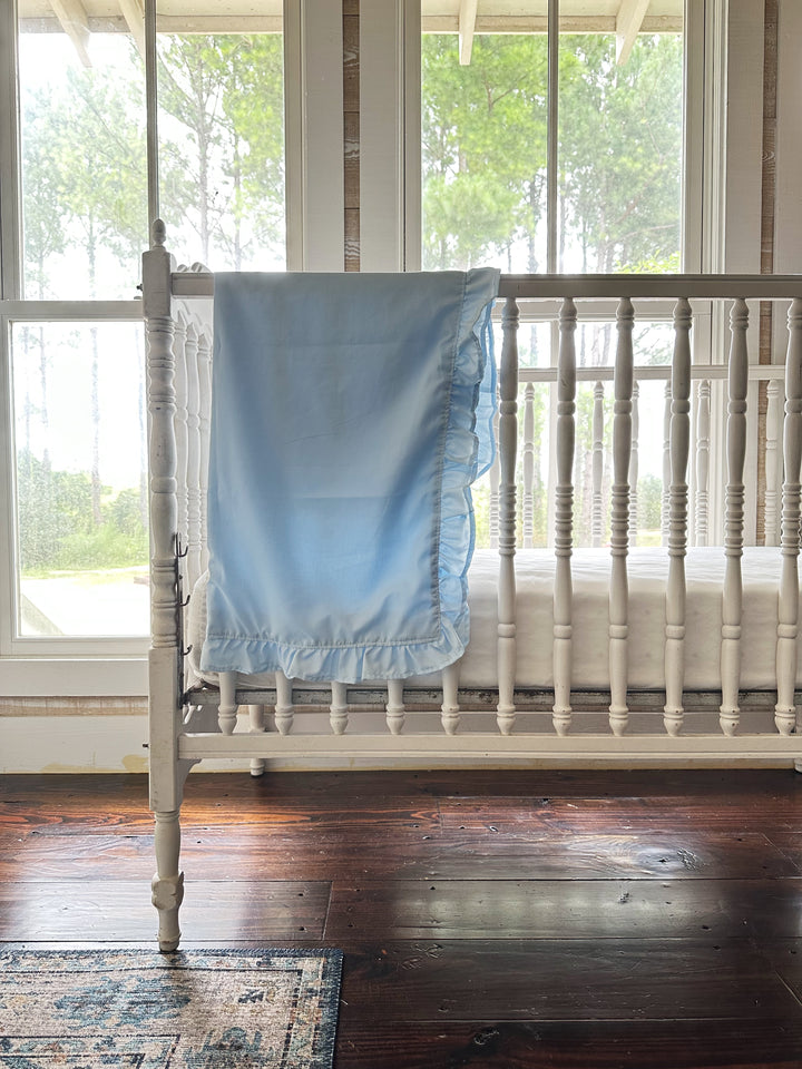 Heirloom blue ruffled crib blanket draped over a white spindle crib in a farmhouse nursery - High Cotton Textile